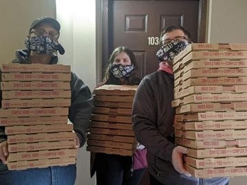 Three people holding 30 pizzas.